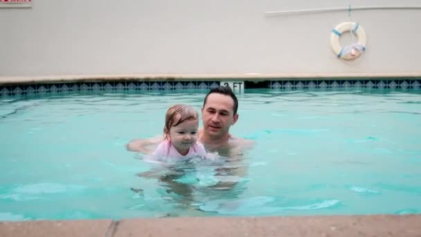 Nette kleine Tochter und sein Vater schwimmen im Pool. Der Vater hält seine Tochter in den Händen und umarmt sie. Zeitlupenaufnahmen — Stockvideo