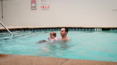 Şirin küçük kızı ve babası havuzda yüzüyorlar. Baba, kızını elinde tutuyor ve ona sarılıyor. Yavaş çekim görüntüleri