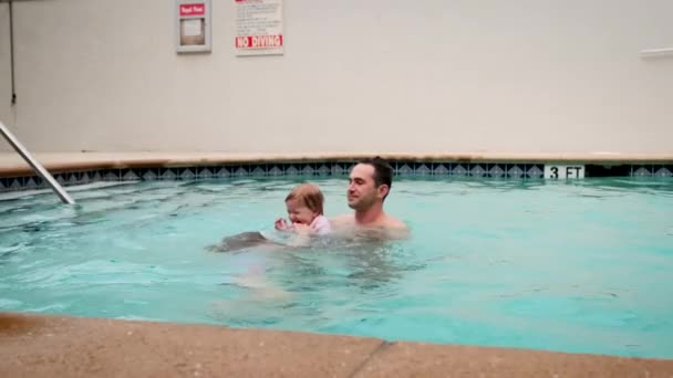 Nette kleine Tochter und sein Vater schwimmen im Pool. Der Vater hält seine Tochter in den Händen und umarmt sie. Zeitlupenaufnahmen — Stockvideo