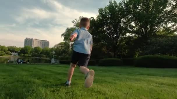 Der Junge rennt auf den Rasen im Park — Stockvideo