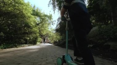 Küçük çocuk güneşli bir günde parkta scooter sürüyor. arka plan