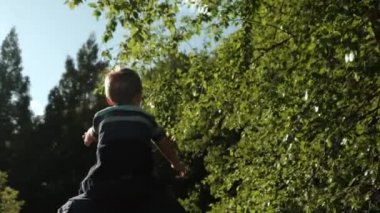 Yürüyen mutlu bir aile. Küçük çocuk babasının omuzlarında parkta yürüyor.