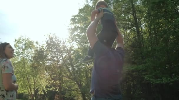 Ходити щасливою сім'єю. Маленький хлопчик сидить на плечах, ходячи в парку. крупним планом — стокове відео