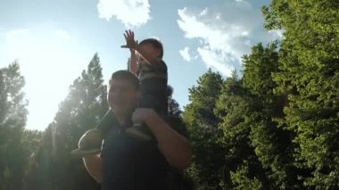 Yürüyen mutlu bir aile. Küçük çocuk babasının omuzlarında parkta yürüyor. Yavaş çekim