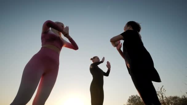 明るいオレンジ色の夕日の空のグループの背景に女性はヨガマットの上に立つと日没で屋外ヨガストレッチ運動を練習 — ストック動画