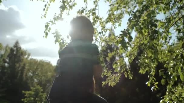 Lopende gelukkige familie. Kleine jongen die op zijn vaders schouders zit en in het park loopt. Langzame beweging — Stockvideo