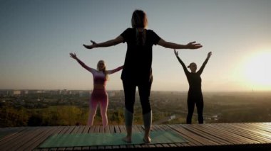 Parlak turuncu günbatımı gökyüzü grubu Womans 'ın arka planına karşı Gün batımında açık havada yoga esneme egzersizi yapıyorlar.
