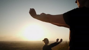 Parlak turuncu günbatımı gökyüzü grubunun arka planında kadınlar gün batımında dışarıda yoga esneme egzersizi yapıyorlar. Görüntüleri kapatın.