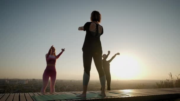 Ευρύ πλάνο του Με φόντο το φωτεινό πορτοκαλί ηλιοβασίλεμα ομάδα ουρανό Womans εξάσκηση .yoga τεντώνοντας άσκηση σε εξωτερικούς χώρους στο ηλιοβασίλεμα — Αρχείο Βίντεο
