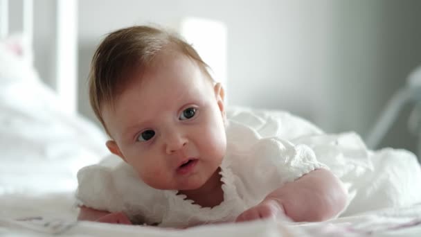 Bebeğin yakın görüntüsü yatakta uzanıyor ve kameraya gülümsüyor. — Stok video