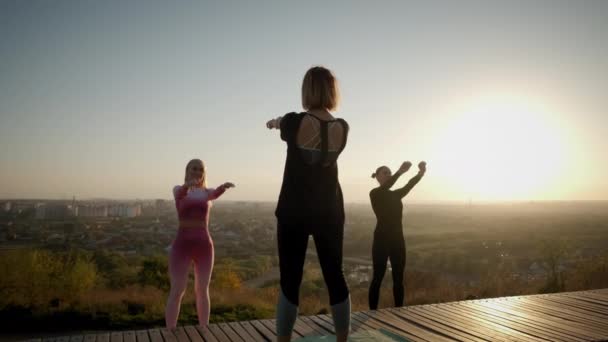 Brede vew van Tegen de achtergrond van de heldere oranje zonsondergang luchtgroep Womans oefenen .yoga stretching oefening buiten in zonsondergang — Stockvideo