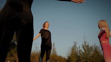 Parlak turuncu günbatımı gökyüzü grubunun arka planında kadınlar açık havada yoga esneme egzersizi yapıyorlar.