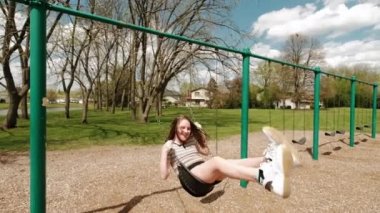 Kız salıncakta sallanıyor ve parkta mutlu bir şekilde gülümsüyor. Geniş açı