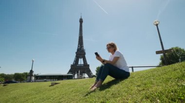 Gündüz vakti Paris 'te Eyfel Kulesi' nin yanında oturan bir kadın akıllı telefon kullanarak selfie çekiyor. Yüksek kalite 4k görüntü