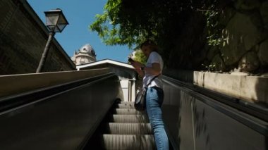 Genç turist kadın, metro istasyonunda ağır çekimde modern yürüyen merdivene binerken arkasına bakıyor. Yüksek kalite 4k görüntü