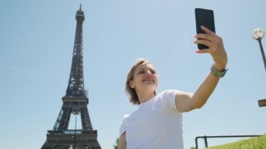 Gündüz vakti Paris 'te Eyfel Kulesi' nin yanında oturan bir kadın akıllı telefon kullanarak selfie çekiyor. Yüksek kalite 4k görüntü