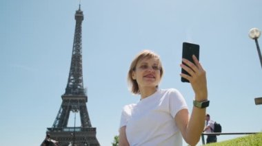 Gündüz vakti Paris 'te Eyfel Kulesi' nin yanında oturan bir kadın akıllı telefon kullanarak selfie çekiyor. Yüksek kalite 4k görüntü