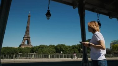 Kadın, Paris 'te gündüz vakti Eyfel Kulesi' nde akıllı telefon kullanarak selfie çekiyor. Yüksek kalite 4k görüntü