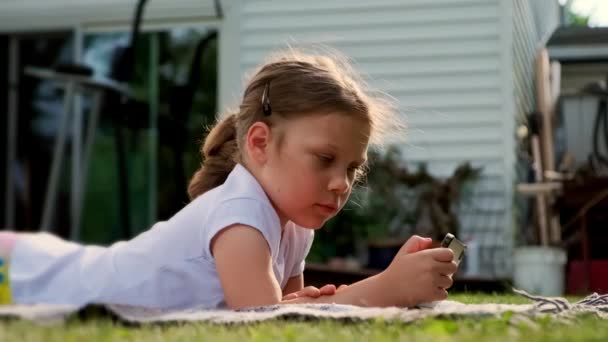 无忧无虑的女孩在玩平板电脑 躺在房子附近的草地上 阳光照射着她的头发 高质量的4K镜头 — 图库视频影像
