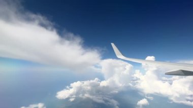 Wing of flying above soft fluffy clouds airplane as seen by passenger through porthole. High quality 4k footage