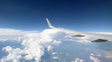 Wing of flying above soft fluffy clouds airplane as seen by passenger through porthole. High quality 4k footage