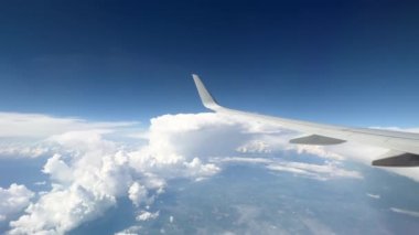 Wing of flying above soft fluffy clouds airplane as seen by passenger through porthole. High quality 4k footage