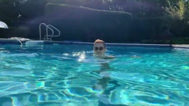 Güneşli bir günde arka bahçedeki havuzda yüzmeye karşı bir kadın. Yüksek kalite 4k görüntü