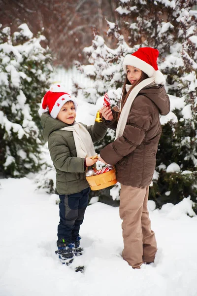 Cute happy kids, boy and girl in santa hats decorate christmas tree in snowy forest. Nice snowy weather Family vacation