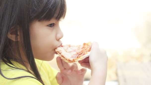 Pequeña chica asiática comiendo una rebanada de pizza — Vídeo de stock