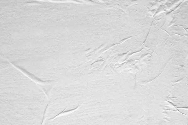 Blank white crumpled and creased paper. White sheet of crumpled paper glued to the wall. Beautiful abstract artistic white empty street poster paper texture pattern