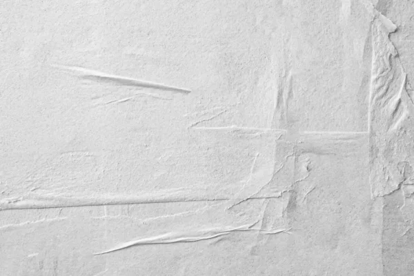 Blank white crumpled and creased paper. White sheet of crumpled paper glued to the wall. Beautiful abstract artistic white empty street poster paper texture pattern