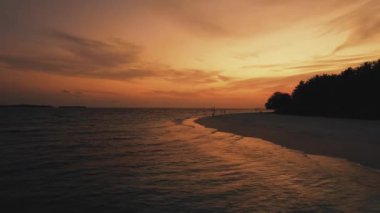 Maldivler 'in okyanus ve ada üzerinde gün batımını gösteren drone görüntüsü, panoramik turuncu gökyüzü