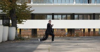 Attractive businesswoman in formal black suit is dancing outside the office, financial district, modern constructivist building on background. The concept of urban city scene.