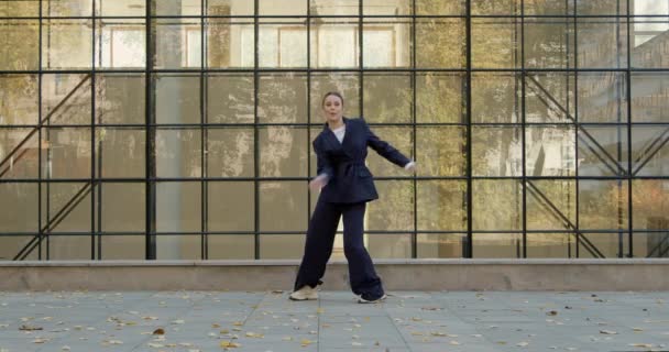 Attractive businesswoman in formal black suit is dancing outside the office, financial district, glass wall on background. The concept of urban city scene. — Video Stock