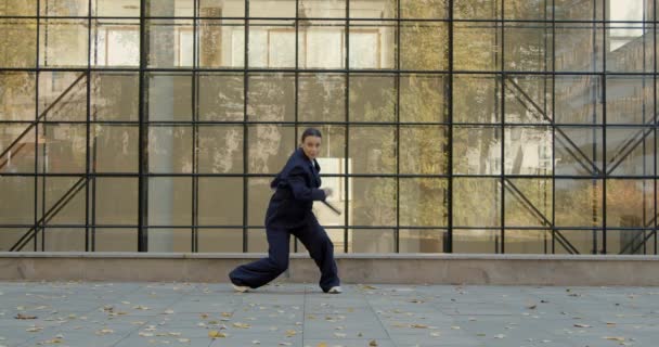 Attractive businesswoman in formal black suit is dancing outside the office, financial district, glass wall on background. The concept of urban city scene. — Video Stock