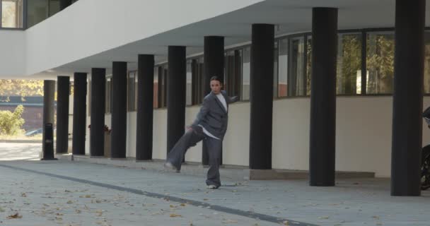 Attractive businesswoman in formal grey suit is dancing outside the office, financial district, modern constructivist building with columns on background. The concept of urban city scene. — Stockvideo