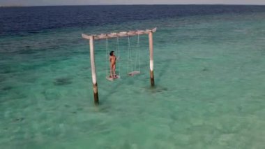 Salıncakta sallanan genç bir kadının, okyanus manzarası. Hint okyanusu, ada ve ufuk çizgisinin göz kamaştırıcı manzarası. Üst düzey seyahat hedefi kavramı