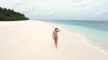 Genç bir kadının Maldivler 'de tropikal ormanlı Hint Okyanusu' nun ufuk çizgisi ve turkuaz dalgaları üzerinde yürüdüğü hava görüntüleri. Turizm ve hafta sonu kavramı