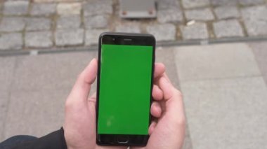 Akıllı telefonu yeşil ekranlı kapat. Telefondaki krom anahtar, alet kullanan eller. Arka planda sokak.