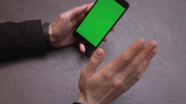 Akıllı telefonu yeşil ekranlı kapat. Telefondaki krom anahtar, alet kullanan eller. Arkaplanda masa.