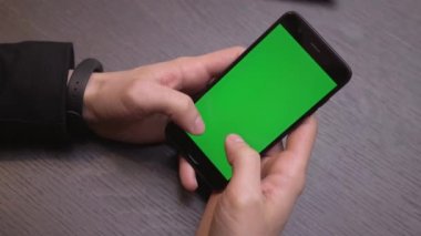 Akıllı telefonu yeşil ekranlı kapat. Telefondaki krom anahtar, alet kullanan eller. Arkaplanda masa.