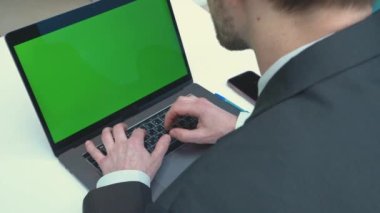 Dizüstü bilgisayarda yazan ve yeşil ekrana bakan bir iş adamının omzunun üstünden. Ofisteki kişi bilgisayar, kromo anahtar ekranı kullanıyor