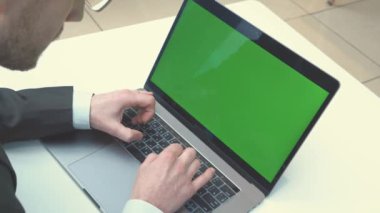 Dizüstü bilgisayarda yazan ve yeşil ekrana bakan bir iş adamının omzunun üstünden. Ofisteki kişi bilgisayar, kromo anahtar ekranı kullanıyor