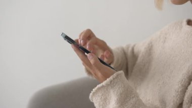 Yan görüş. El ele tutuşan ve evdeki beyaz odada akıllı telefon kullanan bir kadın internete mesaj yazıyor. Kapat..