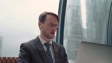 İş adamı bir video konferansında konuşuyor, çevrimiçi iletişim, çalışma süreci, dışarıda yağmurlu ve bulutlu.