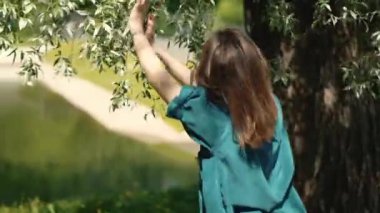 Kadın şehir parkında ağaçların yapraklarıyla dans ediyor ve elleriyle dokunuyor. Gerçek zamanlı çekim. Rahatla ve aromaterapi.