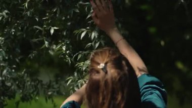 Kadın şehir parkında ağaçların yapraklarıyla dans ediyor ve elleriyle dokunuyor. Gerçek zamanlı çekim. Rahatla ve aromaterapi.