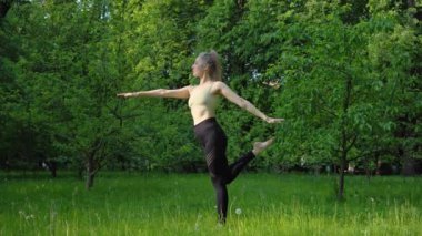 Genç ve formda bir kadın sabah vakti parkta yoga yapıyor. Güzel kız dışarıda yoga egzersizi yapıyor. Gerçek zamanlı.