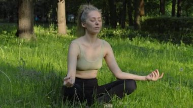 Genç ve formda bir kadın sabah vakti parkta yoga yapıyor. Güzel kız dışarıda yoga egzersizi yapıyor. Gerçek zamanlı.