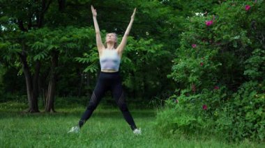 Genç ve formda bir kadın sabah vakti parkta yoga yapıyor. Güzel kız dışarıda yoga egzersizi yapıyor. Gerçek zamanlı.
